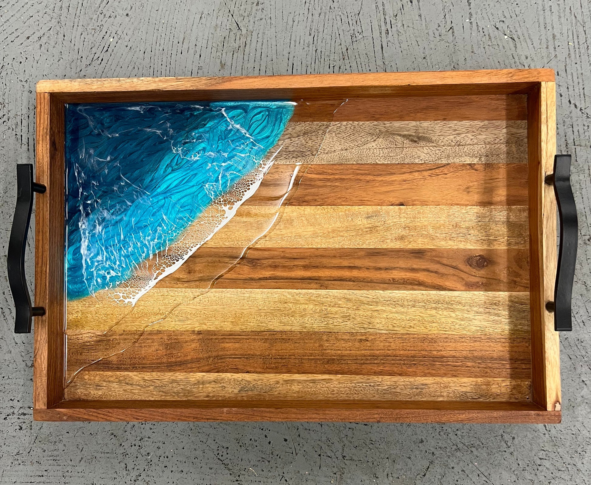 Wooden tray with a blue resin design on a gray textured background