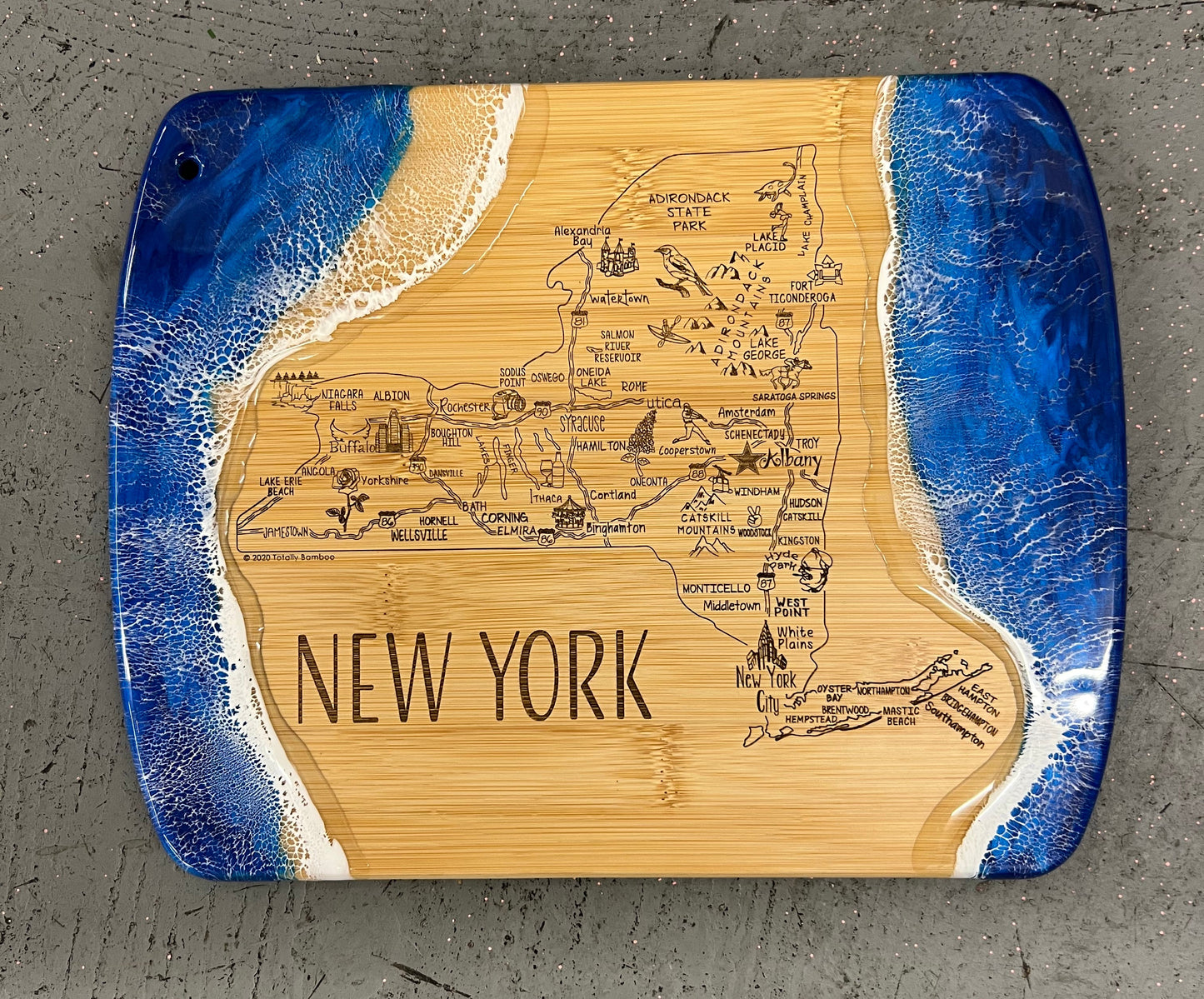 Wooden cutting board with engraved map and 'New York' text, surrounded by blue resin on a gray surface.