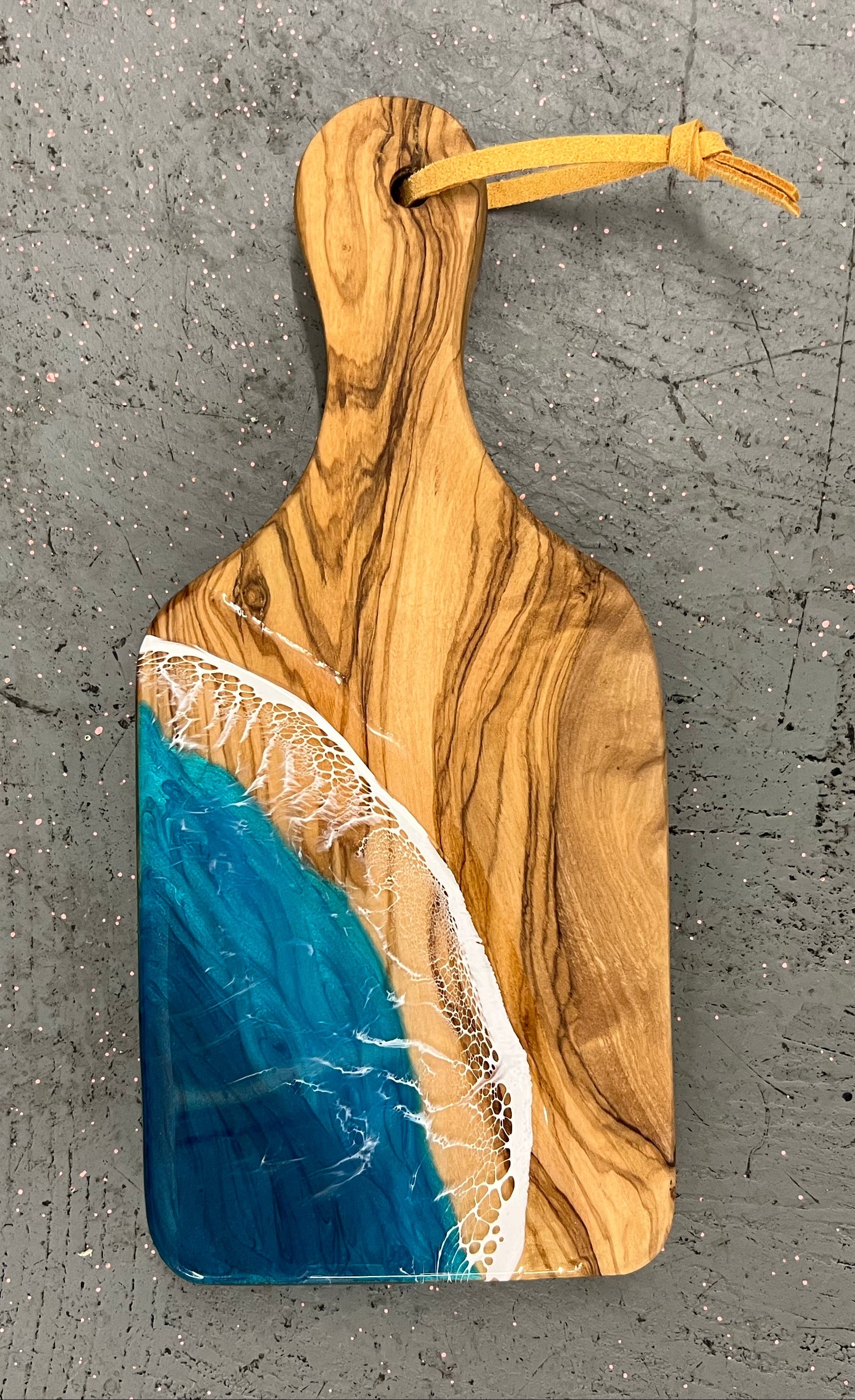 Wooden cutting board with blue resin design on a gray surface